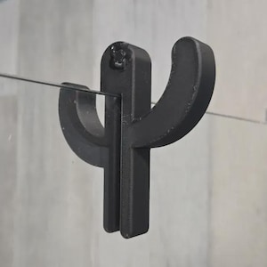 Puede incluir: Un gancho para puerta de ducha de metal negro con forma de cactus. El gancho está montado en una puerta de ducha de cristal. El diseño del cactus tiene dos brazos curvos y un tallo vertical. El gancho está diseñado para sujetar una toalla u otros artículos de baño.