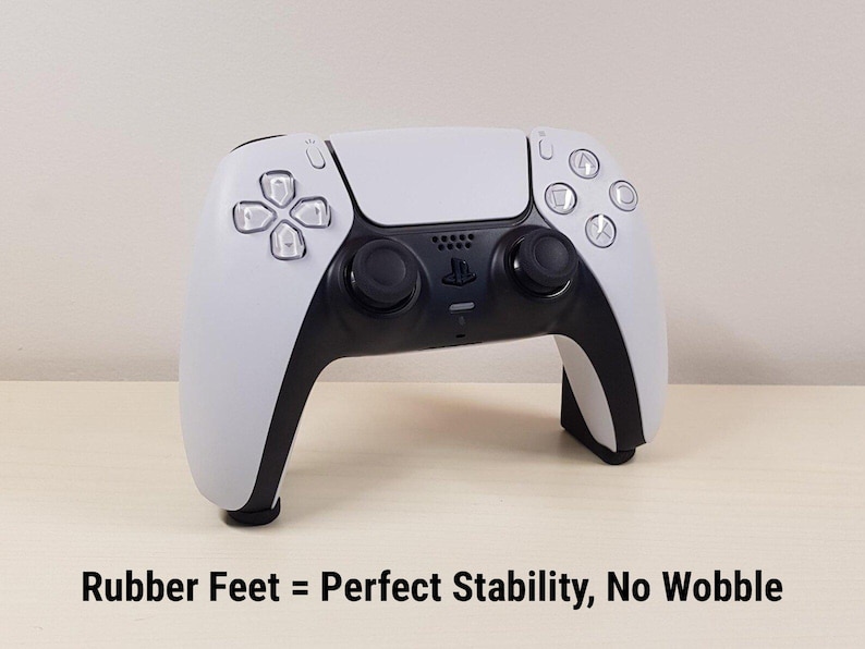 Może przedstawiać: Biało-czarny kontroler do gier z przyciskami i joystickami. Kontroler ma elegancki design z czarną środkową częścią i białymi bokami. Tekst na dole brzmi "Rubber Feet = Perfect Stability, No Wobble."