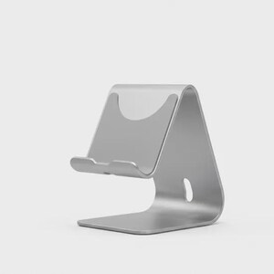 May include: A silver-colored phone stand with a curved design. The stand has a base, a back support, and a small ledge to hold a phone. The stand is made of metal and has a smooth finish.