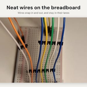 May include: A white breadboard with multiple colored wires including orange, yellow, green, white, and blue, organized by black plastic wire management clips. The text reads: Neat wires on the breadboard. Wires snap in and out, and stay in their lanes.