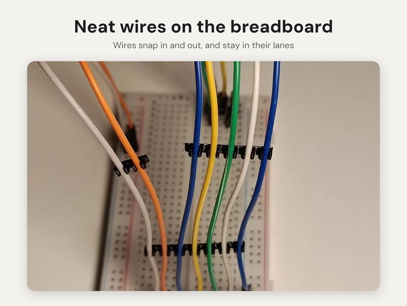 May include: A white breadboard with multiple colored wires including orange, yellow, green, white, and blue, organized by black plastic wire management clips. The text reads: Neat wires on the breadboard. Wires snap in and out, and stay in their lanes.