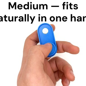 May include: A blue fidget toy with a circular button and a hole, held in a hand. The text "Medium - fits naturally in one hand" is above the toy. The toy is designed to fit comfortably in the hand.