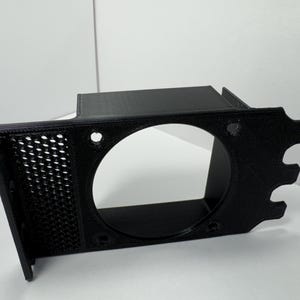 May include: A black 3D-printed bracket with a large circular opening and a perforated side panel. The bracket has several mounting holes and a unique, stylized edge design. The object is made of black plastic.