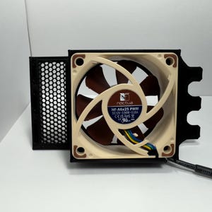 May include: A computer fan with a beige and brown fan blade design. The fan has a black frame and a black mesh filter. The fan has the text "noctua" and "NF-A6x25 PWM" printed on it.