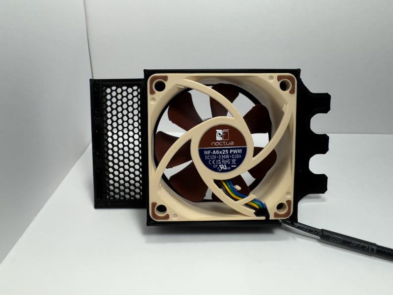May include: A computer fan with a beige and brown fan blade design. The fan has a black frame and a black mesh filter. The fan has the text "noctua" and "NF-A6x25 PWM" printed on it.