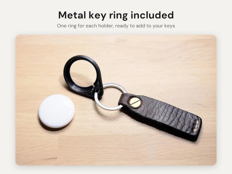 May include: A white circular tracking device next to a dark brown leather keychain with a brass rivet and a silver metal key ring. The text Metal key ring included and One ring for each holder, ready to add to your keys is visible.