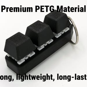 K&ouml;nnte beinhalten: Ein schwarzer Schl&uuml;sselanh&auml;nger mit drei strukturierten, quadratischen Tasten. Die Tasten sind auf einer schwarzen Basis mit wei&szlig;en Halterungen angebracht. Der Text "Premium PETG Material" und "Strong, lightweight, long-lasting" ist sichtbar.