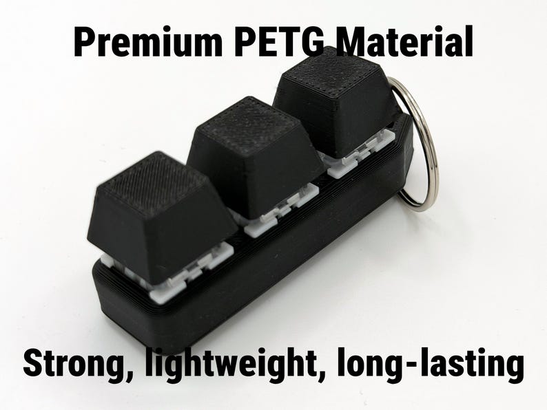 K&ouml;nnte beinhalten: Ein schwarzer Schl&uuml;sselanh&auml;nger mit drei strukturierten, quadratischen Tasten. Die Tasten sind auf einer schwarzen Basis mit wei&szlig;en Halterungen angebracht. Der Text "Premium PETG Material" und "Strong, lightweight, long-lasting" ist sichtbar.