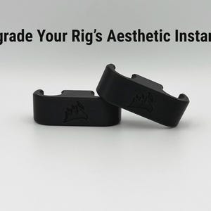 May include: Two black computer component accessories are shown against a white backdrop. The text "Upgrade Your Rig's Aesthetic Instantly" is above the components. The accessories are curved and feature a logo. They have a slot on top.