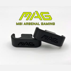 May include: Two black gaming accessories, each with the word "MAG" embossed. The accessories are on a white surface, with the text "MAG MSI ARSENAL GAMING" in green above them.
