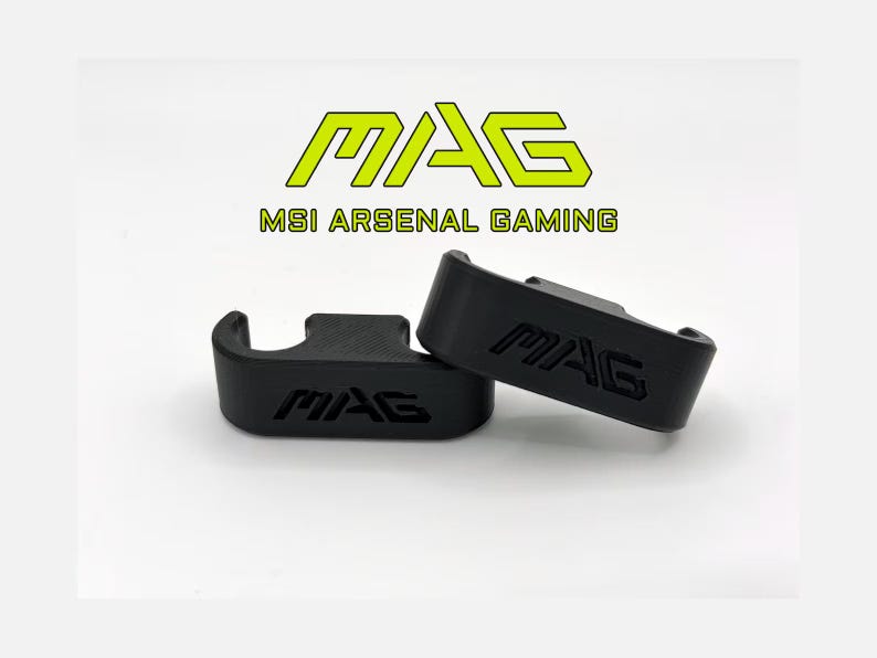 May include: Two black gaming accessories, each with the word "MAG" embossed. The accessories are on a white surface, with the text "MAG MSI ARSENAL GAMING" in green above them.