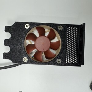 May include: A black computer fan assembly with a brown fan and a black mesh cover. The fan is secured with four screws. The assembly has a unique shape with a curved edge and a wire extending from it.