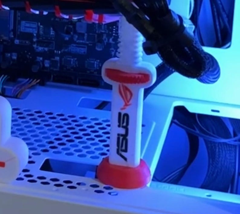 Pode incluir: Um parafuso branco e vermelho para caixa de PC ASUS ROG. O parafuso tem uma base e um topo vermelhos, com o logotipo e o texto ASUS ROG em branco. O parafuso foi projetado para fixar componentes dentro de uma caixa de computador.