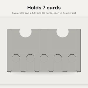 May include: A light gray memory card holder featuring text that reads Holds 7 cards, 5 microSD and 2 full-size SD cards, each in its own slot. The rectangular organizer has two large semi-circular cutouts at the top and five smaller circular slots at the bottom.