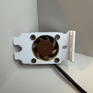 May include: A white computer fan with a brown fan blade and a black cable. The fan is attached to a white bracket with four screws. The fan is designed to cool computer components.