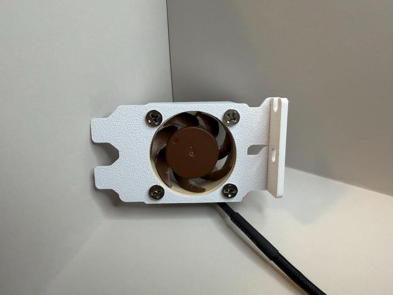 May include: A white computer fan with a brown fan blade and a black cable. The fan is attached to a white bracket with four screws. The fan is designed to cool computer components.
