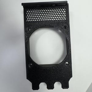 May include: A black, rectangular plastic component with a large circular opening and a mesh screen at the top. The component has several small holes and three rounded protrusions at the bottom.