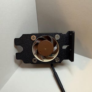 May include: A black computer fan with a brown central element and four silver screws. The fan is mounted on a black bracket with a cable extending from the bottom. Designed for computer cooling.