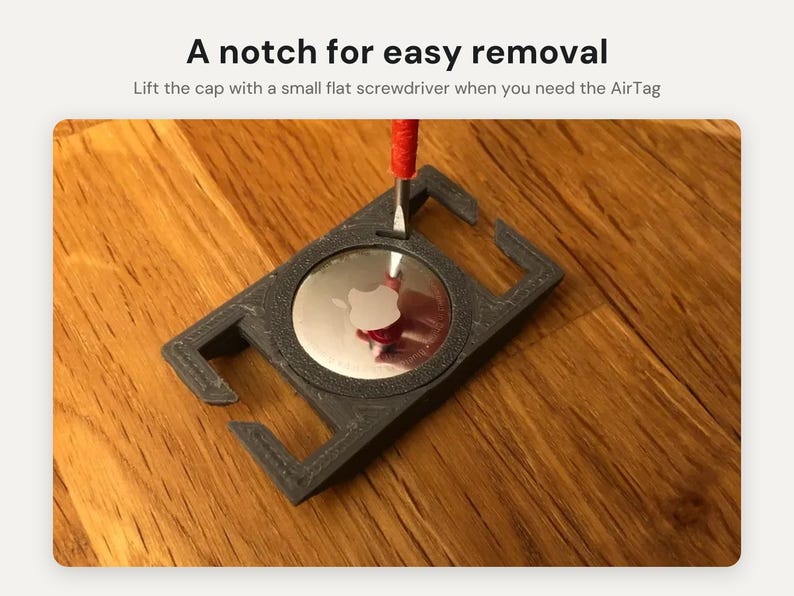 May include: A dark gray rectangular holder for an Apple AirTag with a central circular cutout. A small flathead screwdriver is inserted into a notch on the holder. Text reads: A notch for easy removal. Lift the cap with a small flat screwdriver when you need the AirTag.