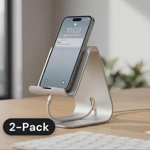 May include: A silver-colored metal smartphone stand with a triangular profile, holding a smartphone with a digital display showing the time 10:09. A white charging cable is connected to the device. The text 2-Pack is visible in the corner.