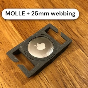 May include: A black 3D-printed mount for an Apple AirTag, featuring a circular center cutout and side slots for attachment. The mount is labeled with the text "MOLLE + 25mm webbing" and is designed to secure an AirTag to gear straps.