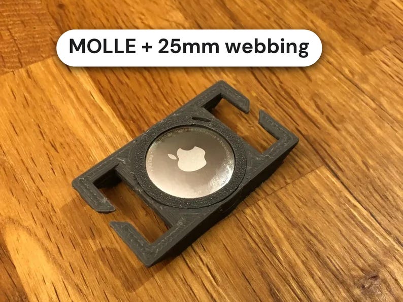 May include: A black 3D-printed mount for an Apple AirTag, featuring a circular center cutout and side slots for attachment. The mount is labeled with the text "MOLLE + 25mm webbing" and is designed to secure an AirTag to gear straps.