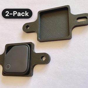 May include: A 2-pack of black, square-shaped plastic mounts with side tabs featuring mounting holes. One mount is empty, showing a textured interior, while the other holds a dark gray square electronic tracker with a circular button.