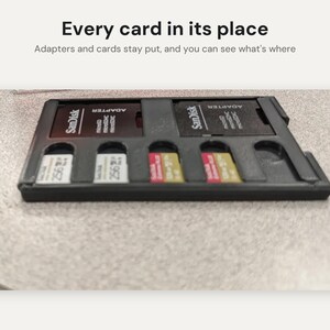May include: A black plastic storage tray for memory cards and adapters. The tray contains two SanDisk adapters and four microSD cards. Text above the tray reads: Every card in its place. Adapters and cards stay put, and you can see what's where.
