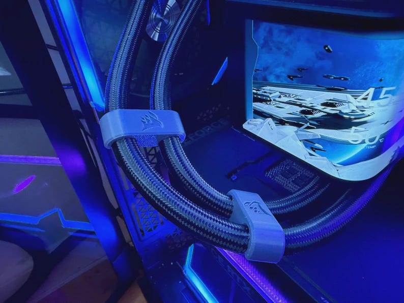 May include: A close-up of a computer's internal components, with a curved monitor showing a futuristic scene. Braided black and grey tubes are held by light grey clips with a logo. The scene is illuminated with blue LED lighting.