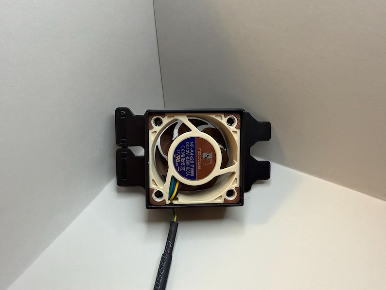 May include: A computer fan with a brown and beige fan blade, a black frame, and a blue and white label. The fan has a black wire and is set against a white background.