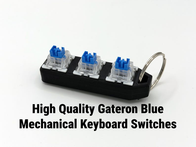 K&ouml;nnte beinhalten: Ein schwarzer, rechteckiger Schl&uuml;sselanh&auml;nger mit drei Gateron Blue mechanischen Tastaturschaltern. Die Schalter haben blaue Stiele und transparente Geh&auml;use. Ein silberner Metallring ist angebracht. Der Text lautet "High Quality Gateron Blue Mechanical Keyboard Switches".