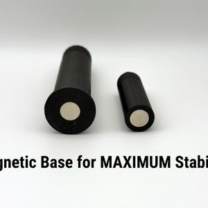 Puede incluir: Dos objetos cil&iacute;ndricos negros con bases magn&eacute;ticas se muestran sobre un fondo blanco. El cilindro m&aacute;s grande tiene una base m&aacute;s ancha. El texto "Magnetic Base for MAXIMUM Stability" est&aacute; en la parte inferior.