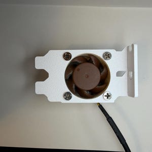 May include: A small computer fan with a brown fan blade and a white metal bracket. The fan is secured with four screws. A black wire extends from the fan.