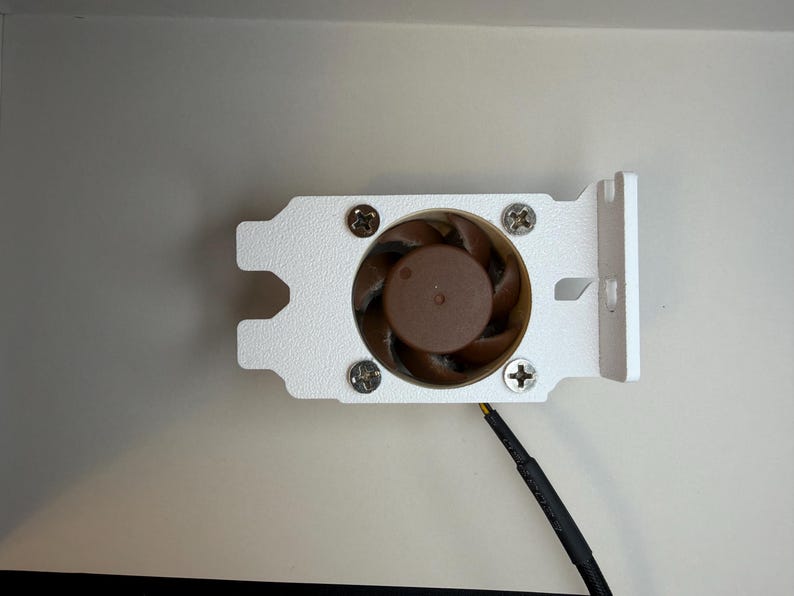 May include: A small computer fan with a brown fan blade and a white metal bracket. The fan is secured with four screws. A black wire extends from the fan.