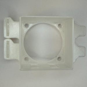 May include: A translucent, square plastic component with a central circular aperture and four small holes. It has two rectangular tabs on one side and two on the opposite. Likely a mounting bracket or housing.