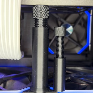 Puede incluir: Primer plano de dos tornillos negros roscados con tapas texturizadas, probablemente para hardware de computadora. Los tornillos son de diferentes tamaños y están colocados frente a un ventilador de computadora y otros componentes internos. Iluminación LED azul visible.