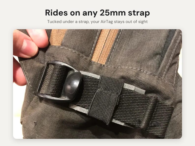 May include: A black plastic AirTag holder attached to a dark gray fabric strap. The text reads: Rides on any 25mm strap. Tucked under a strap, your AirTag stays out of sight. The holder features a black buckle mechanism.