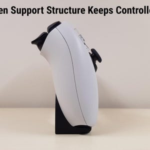 Może przedstawiać: Biały kontroler do gier jest podparty na czarnym stojaku. Kontroler ma czarne przyciski i spusty. Tekst "Hidden Support Structure Keeps Controller Up" znajduje się u g&oacute;ry obrazu.