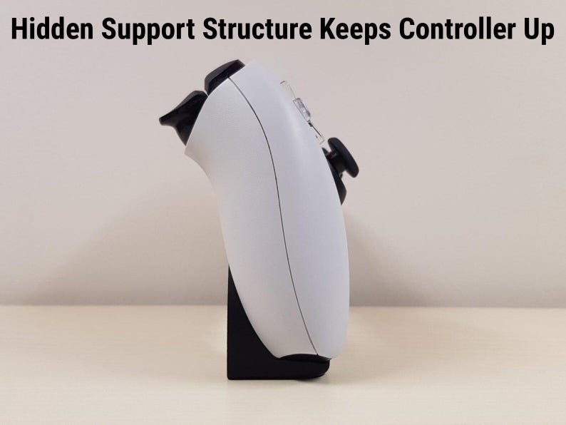 Może przedstawiać: Biały kontroler do gier jest podparty na czarnym stojaku. Kontroler ma czarne przyciski i spusty. Tekst "Hidden Support Structure Keeps Controller Up" znajduje się u g&oacute;ry obrazu.