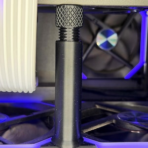 May include: Close-up of a computer's internal components, featuring a black, textured screw with a knurled head. A cylindrical black post extends downward. A fan with a blue and silver center is visible in the background, along with blue LED lighting.