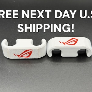 May include: Two white, curved plastic components with a red logo. The components have a rectangular top with a curved base and are set against a dark background. The logo is a stylized red design.