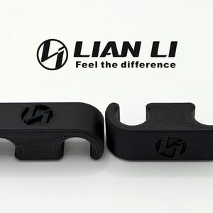 May include: Two black, 3D-printed cable management clips. Each clip features the Lian Li logo. The logo and the text "Feel the difference" are printed above the clips. The clips have a curved design with openings for cables.