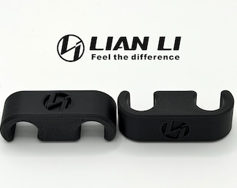 May include: Two black, 3D-printed cable management clips. Each clip features the Lian Li logo. The logo and the text "Feel the difference" are printed above the clips. The clips have a curved design with openings for cables.
