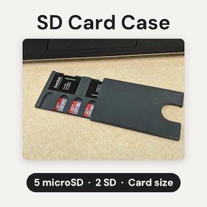 May include: A dark gray SD card case with a sliding cover, designed to hold 5 microSD cards and 2 SD cards. The case features the text SD Card Case at the top and 5 microSD &middot; 2 SD &middot; Card size at the bottom, with visible SanDisk memory cards.