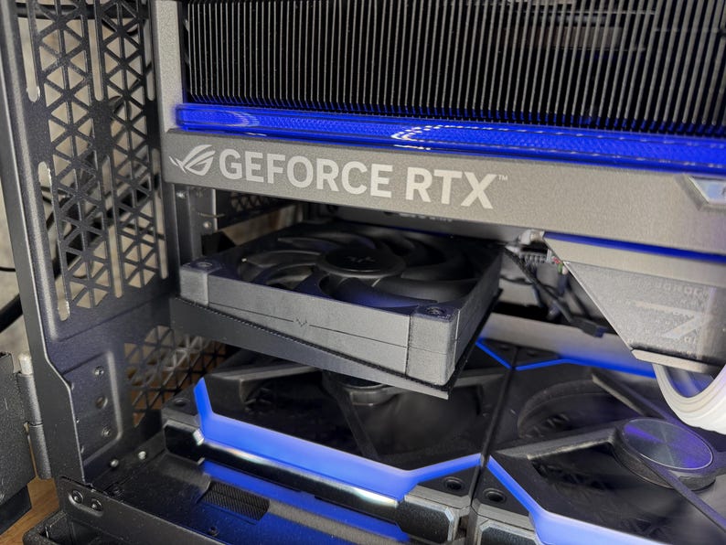 May include: A close-up of a computer component with the text "GEFORCE RTX" in silver. The component has a black fan and blue LED lighting. The computer case has a geometric design.