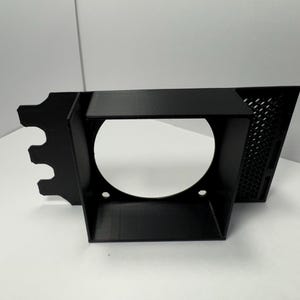 May include: A black, angular bracket with a circular opening and a perforated side panel. The bracket has a series of cutouts on one end and two small holes near the base of the circular opening. The object is set against a white background.