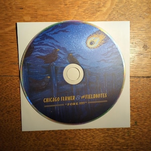 May include: A CD with a blue and gold design featuring black birds perched on a fence under a night sky with a comet. The text "CHICAGO FARMER & THE FIELDNOTES" and "FORE!!!!" is printed on the CD.