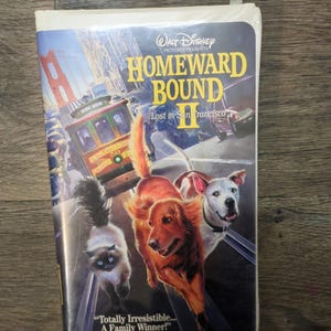 May include: A VHS tape of "Homeward Bound II: Lost in San Francisco" by Walt Disney Pictures. The cover features a cable car, the Golden Gate Bridge, and illustrations of a cat and two dogs. The text reads "Totally Irresistible... A Family Winner!"