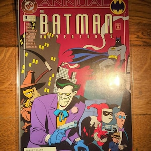 May include: A comic book cover for "The Batman Adventures Annual #1" featuring Batman, The Joker, Harley Quinn, and Scarecrow. The cover has a red background with the title in large, yellow letters. The characters are in a cartoon style.