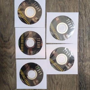 May include: Six compact discs, each in a white paper sleeve, are arranged on a wooden surface. The discs are black with gold centers and feature the text "TUROW" and "REVERSIBLE ERRORS". The discs are labeled "DISC ONE", "DISC TWO", "DISC THREE", and "DISC FOUR".